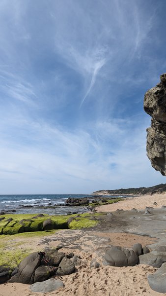 A rocky coastline with moss-covered boulders and a sandy beach under a blue sky. — Benavides, Tarifa, Andalusia, Spain