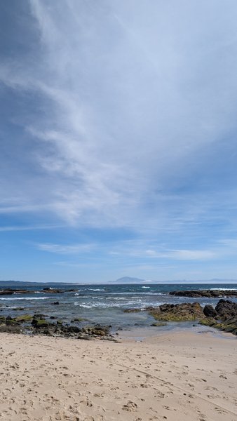 A view from the sandy beach looking out towards the rocky shoreline and the sea under a clear sky. — Benavides, Tarifa, Andalusia, Spain