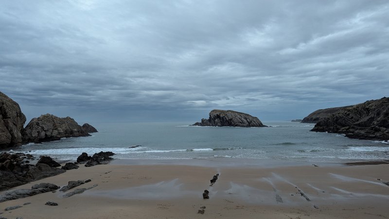 A wide view of a sandy beach with rocky outcrops and calm water under a cloudy sky. — Covachos (Piélagos), Piélagos, Cantabria, Spain