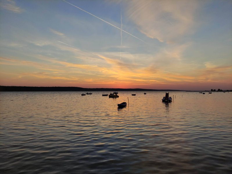 A sunset view across the water with small boats moored in the bay at Ljubač. — Ljubac (Općina Ražanac), Ljubač, Croatia