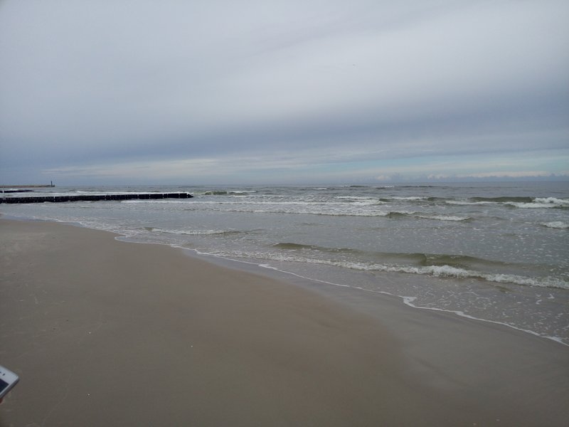 Wide sandy beach and waves at Łeba under an overcast sky.