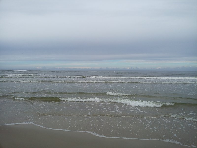 Small waves rolling onto the beach in Łeba under an overcast sky.