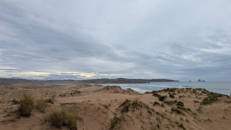 A wide shot of sandy dunes with the ocean and distant cliffs under a cloudy sky. — Liencres (Cantábria), Piélagos, Cantabria, Spain