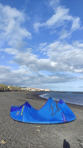 A blue kite rests on the black sand beach at Puerto de Güímar with the coastline in the background. — Puerto de Güímar (Tenerife), Güímar, Canary Islands, Spain