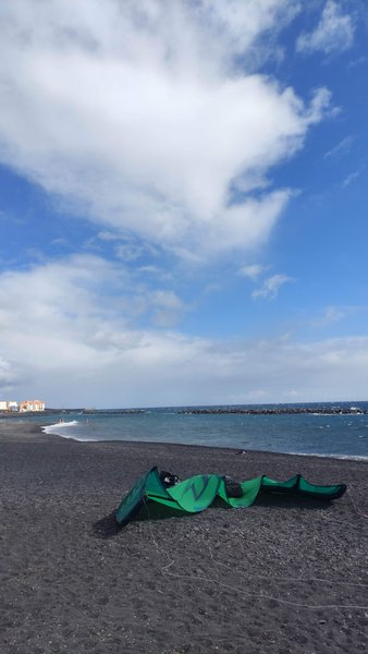 A kite lies on the black sand beach at Puerto de Güímar with the sea and breakwaters in the background. — Puerto de Güímar (Tenerife), Güímar, Canary Islands, Spain