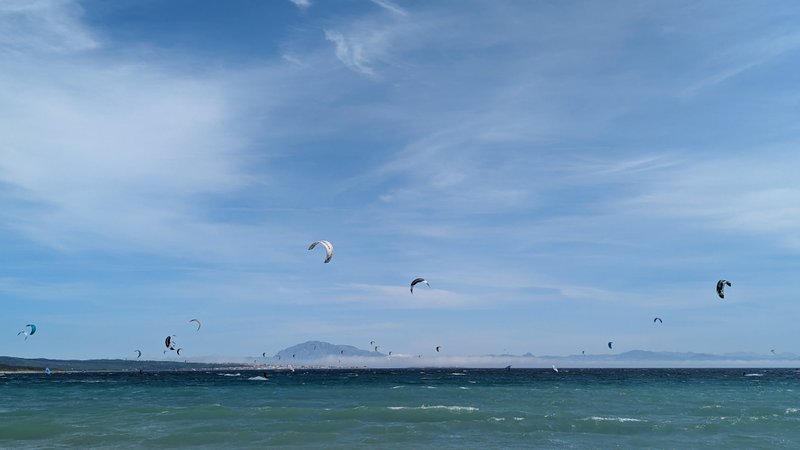 Numerous kitesurfers on the water at Punta Paloma with the Moroccan coastline visible in the distance.