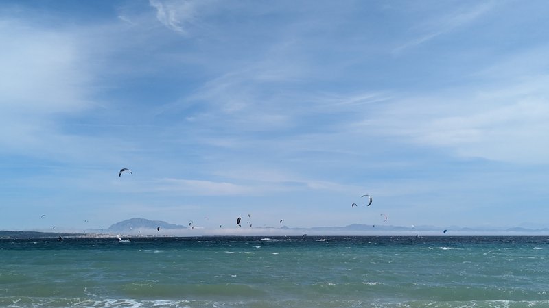 Several kitesurfers on the water at Punta Paloma with mountains in the background.