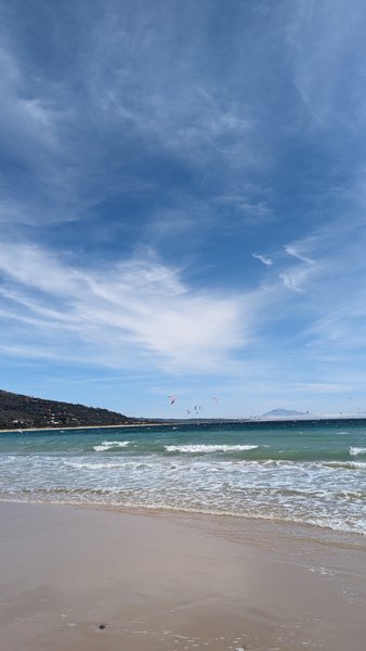 A view of the beach and kitesurfers on the water at Punta Paloma under a blue sky.