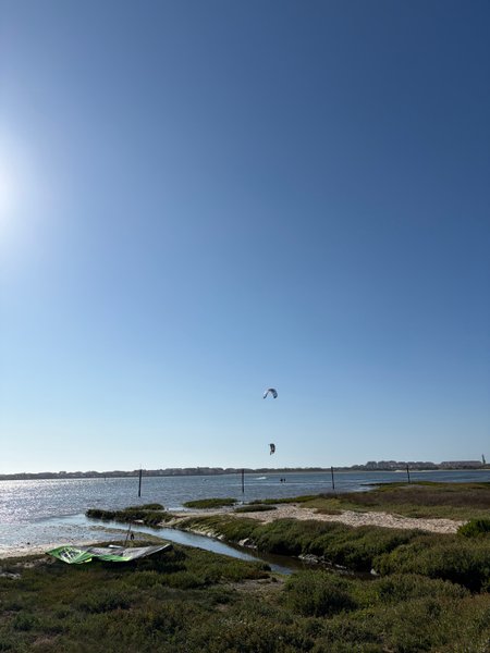 A view of the lagoon at Estacas with kites in the air and gear on the shore. — Estacas (Ria de Aveiro), Ílhavo, Portugal