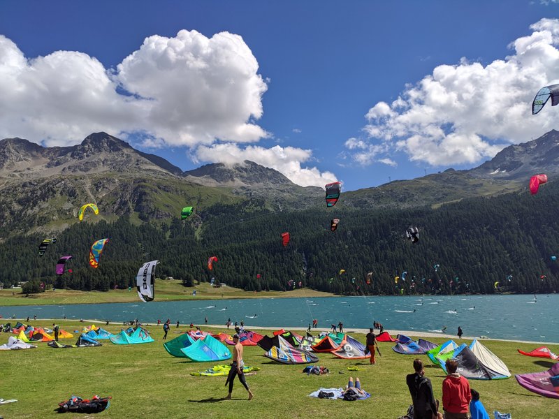 A busy day at Lake Silvaplana with many kites in the air and on the grass launch area. — Silvaplana (Lake Silvaplana), Silvaplana, Switzerland