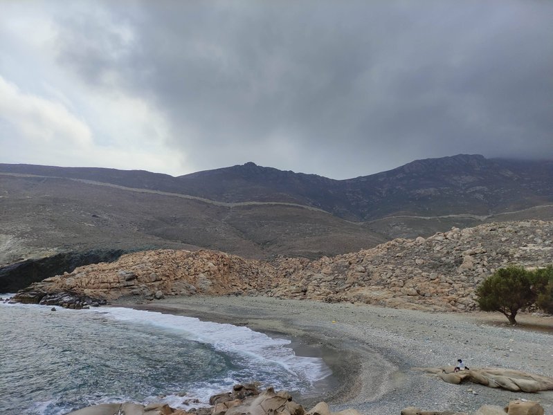 A wide view of the pebble beach and surrounding hills at Leivada under an overcast sky. — Leivada (Tinos), Tinos Regional Unit, South Aegean, Greece