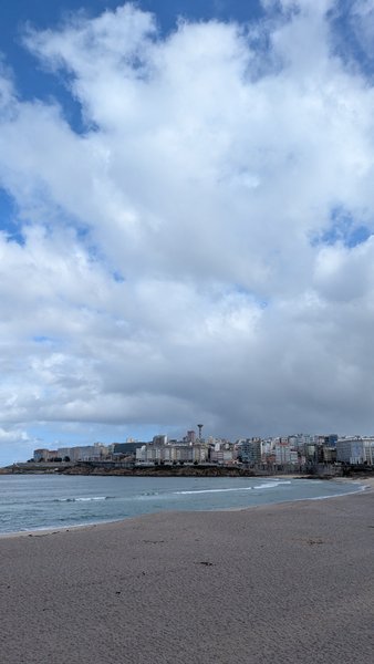A wide view of Playa de Riazor showing the sandy beach, water, and the city skyline of A Coruña.