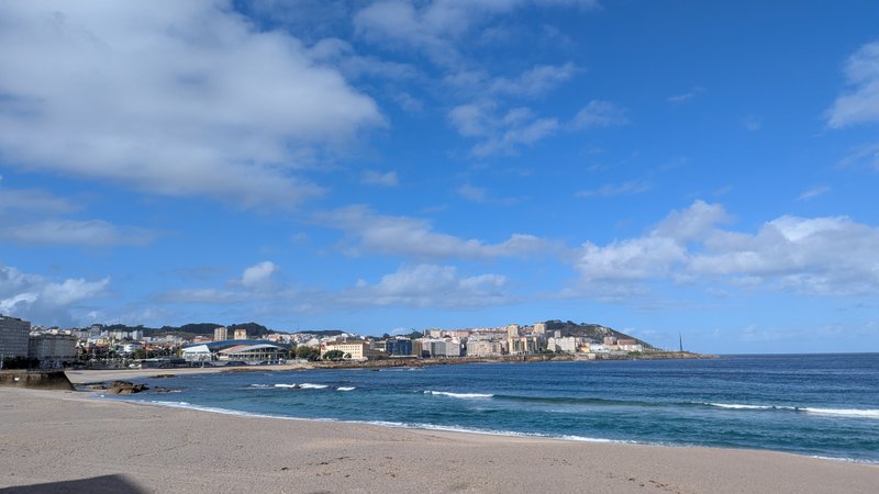 A wide view of Playa de Riazor beach and the water with the city of A Coruña in the background.