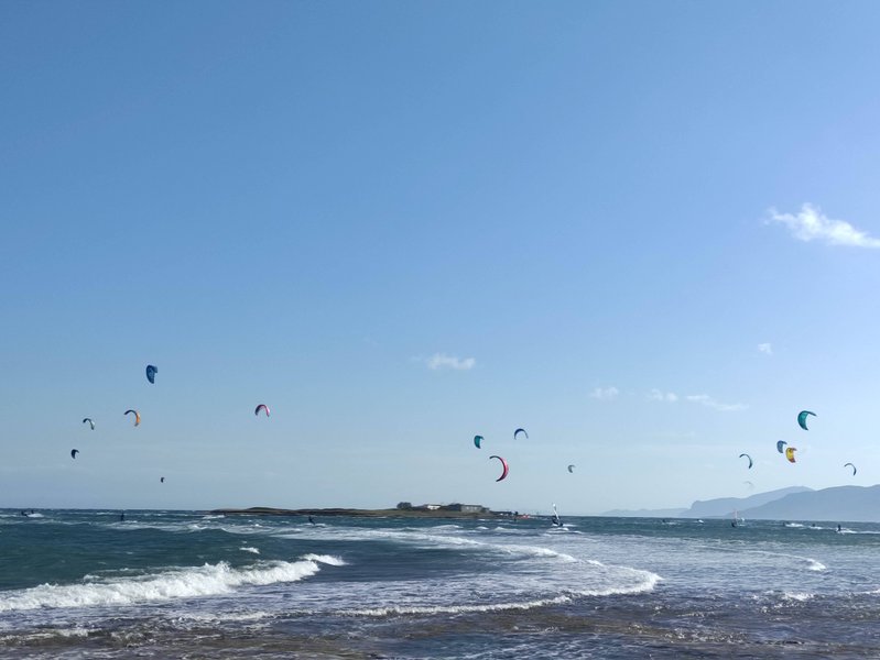 Multiple kitesurfers on the water at Nissakia Loutsa with a small island in the background.