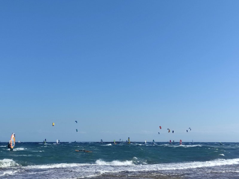 Windsurfers and kitesurfers on the choppy water under a clear blue sky at Nissakia Loutsa.