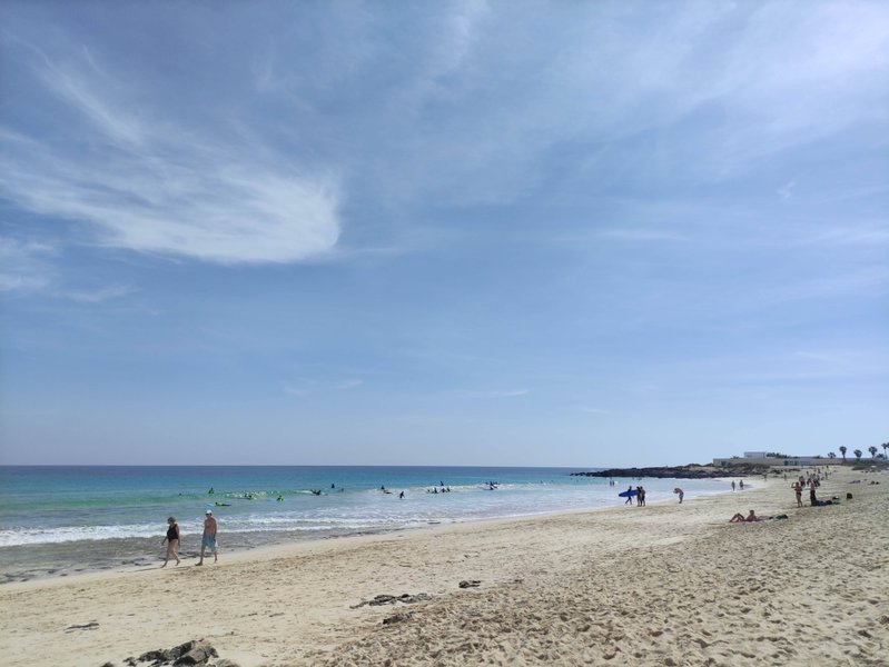 A wide view of the sandy beach and turquoise waters at Los Hoteles with people in the surf. — Los Hoteles (La Oliva–Corralejo), La Oliva, Canary Islands, Spain