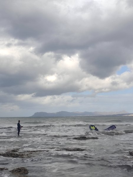 A kiteboarder stands in the waves with a kite in the water at Agia Marina Platanias.