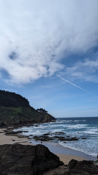 A rocky coastline and sandy beach at Aviño with waves breaking on the shore.
