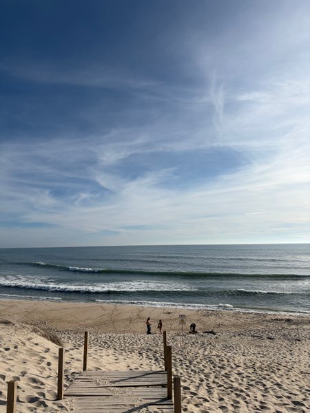 A wide view of Praia do Areão featuring the beach, rolling waves, and a wooden access path.