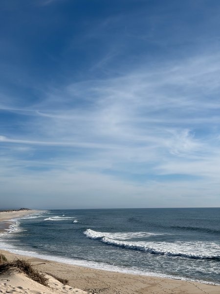 Wide view of the beach and waves at Praia do Areão under a blue sky.
