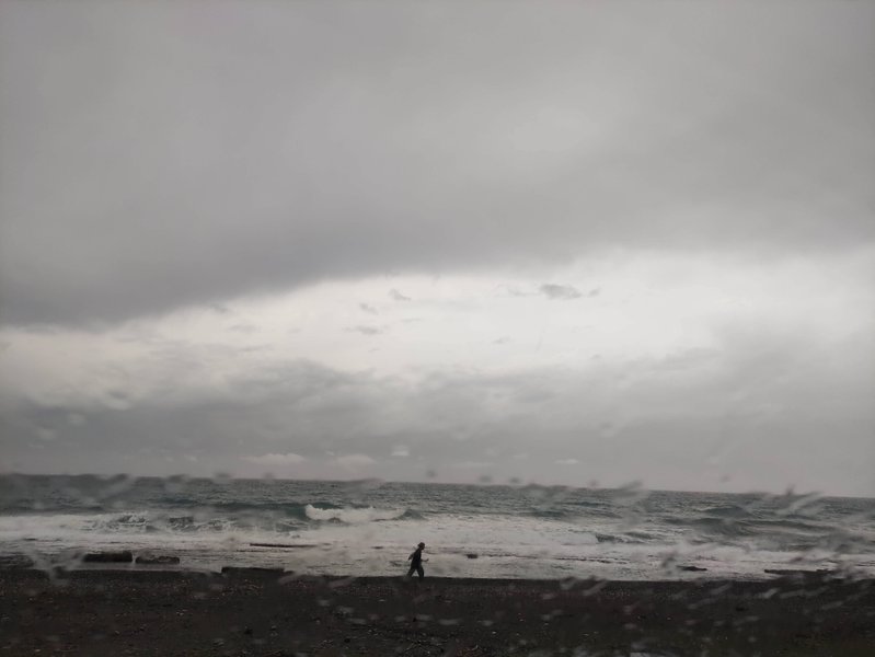 A person walks along a choppy beach under a dark, overcast sky. — Peristeras (Ierapetra Bay), Ierapetra Municipal Unit, Greece