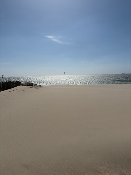 A wide sandy beach with a kitesurfer visible on the water under a clear blue sky. — Praia da Barra (Aveiro), Gafanha da Nazaré, Portugal
