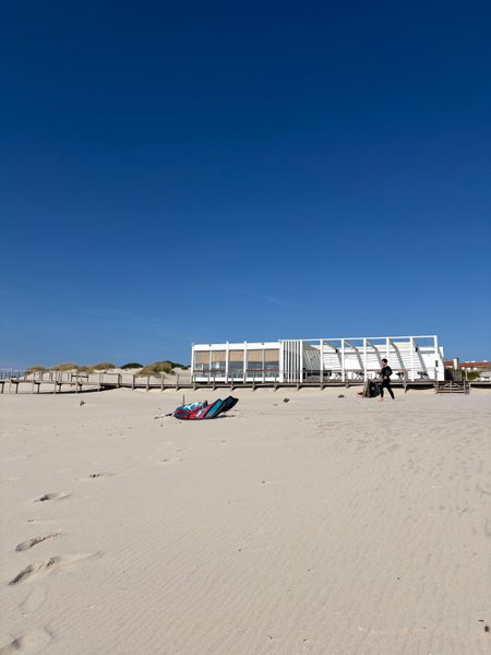 A kite lies on the wide sandy beach in front of a beach bar at Praia da Barra. — Praia da Barra (Aveiro), Gafanha da Nazaré, Portugal