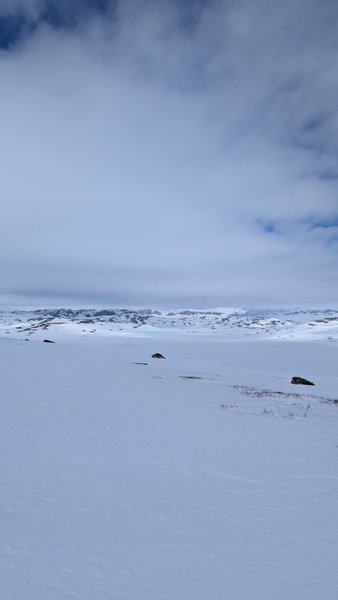 A vast snow-covered plateau with distant mountains under a cloudy sky. — Batstjorn (Planície do Hardangervidda), Norway