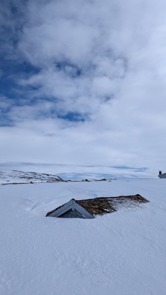 A partially buried building in a vast, snow-covered landscape under a cloudy sky. — Batstjorn (Planície do Hardangervidda), Norway