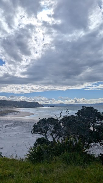A wide view of a sandy beach and ocean with distant hills under a cloudy sky. — Otama, Ōtama, Waikato, New Zealand