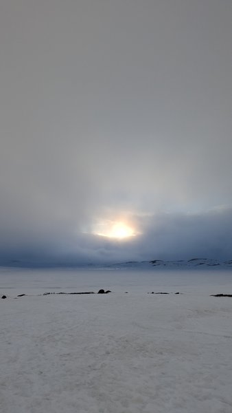 A vast snowy landscape under a cloudy sky with the sun breaking through. — Oerteren, Buskerud, Norway