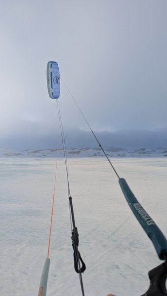 A kite flies above a vast, snow-covered landscape with distant mountains under an overcast sky. — Oerteren, Buskerud, Norway