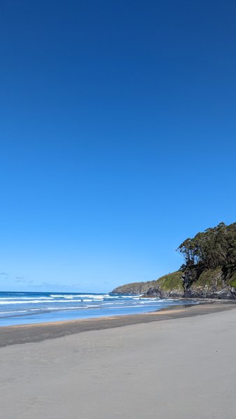 A wide view of the sandy beach and surf at Playa de Otur under a clear blue sky. — Playa de Otur (Otur), Valdés, Asturias, Spain