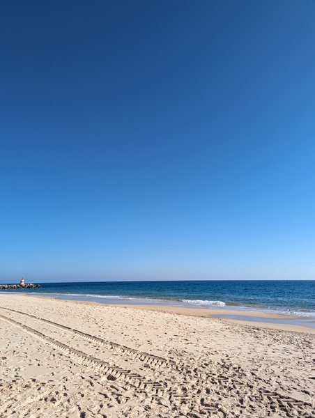 A wide sandy beach at Ilha de Tavira with calm water and a clear sky.