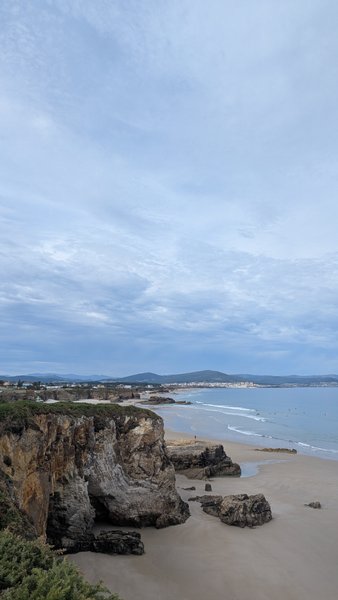 An aerial view of a rugged coastline with cliffs, a sandy beach, and the ocean under a cloudy sky. — San Cosme (Foz), Suigrexa, Galicia, Spain